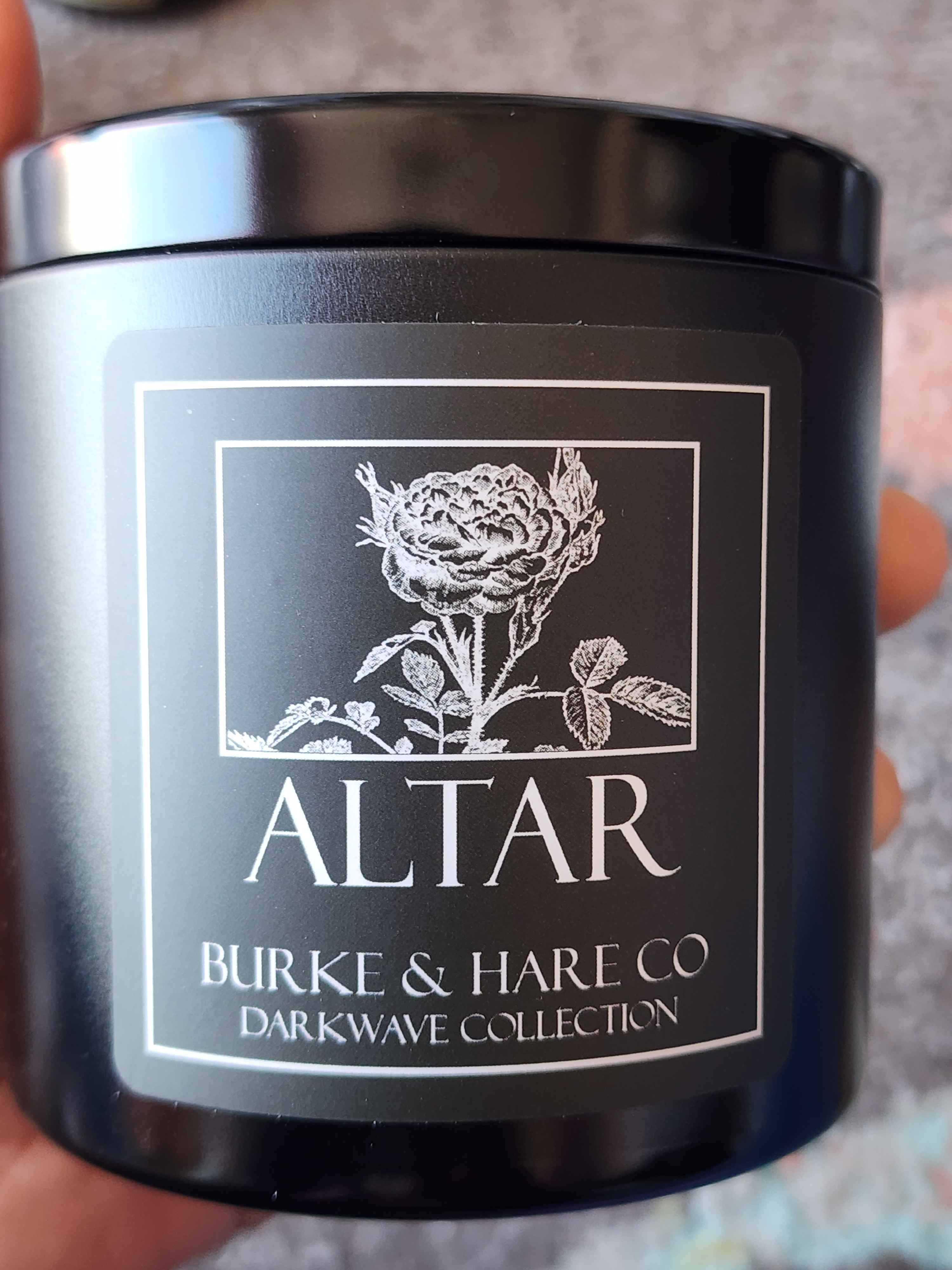 ID: a candle from Burke & Hare's Darkwave collection. the candle is in a black jar with a black label. the white text reads Altar, with a white illustration of a rose