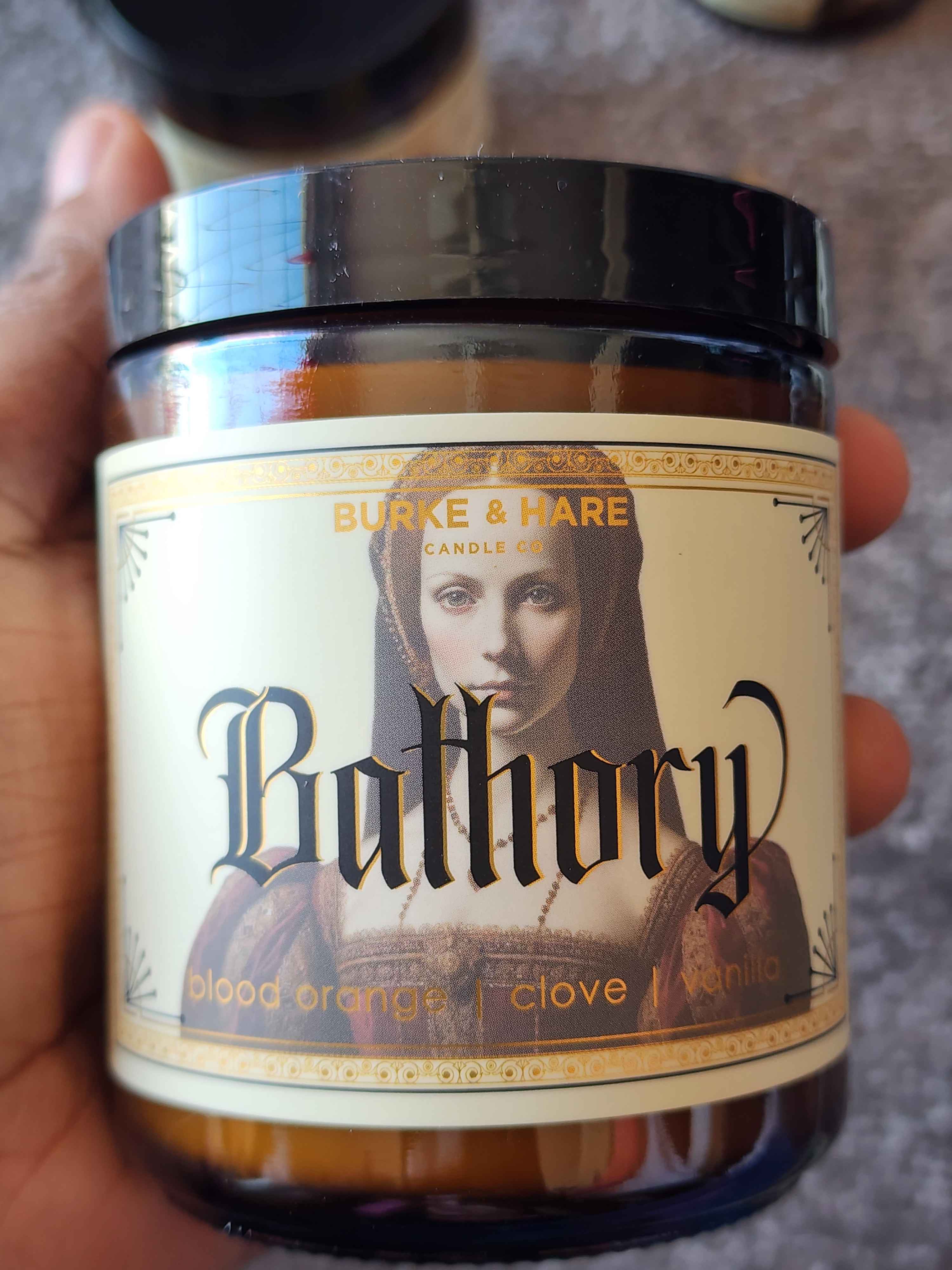 ID: an amber jar candle from Burke & Hare named Bathory, with notes of blood orange, clove, and vanilla