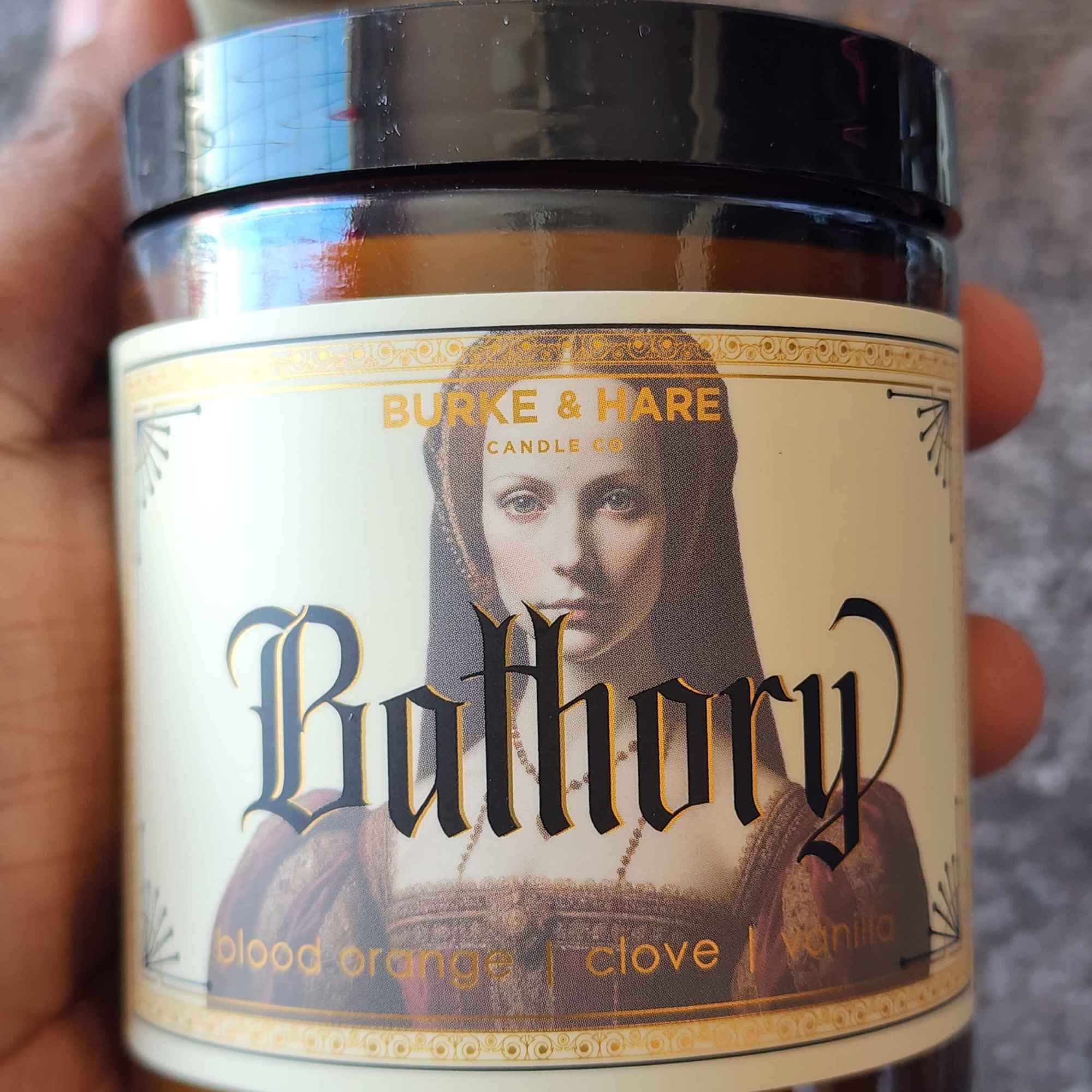 ID: an amber jar candle from Burke & Hare named Bathory, with notes of blood orange, clove, and vanilla 