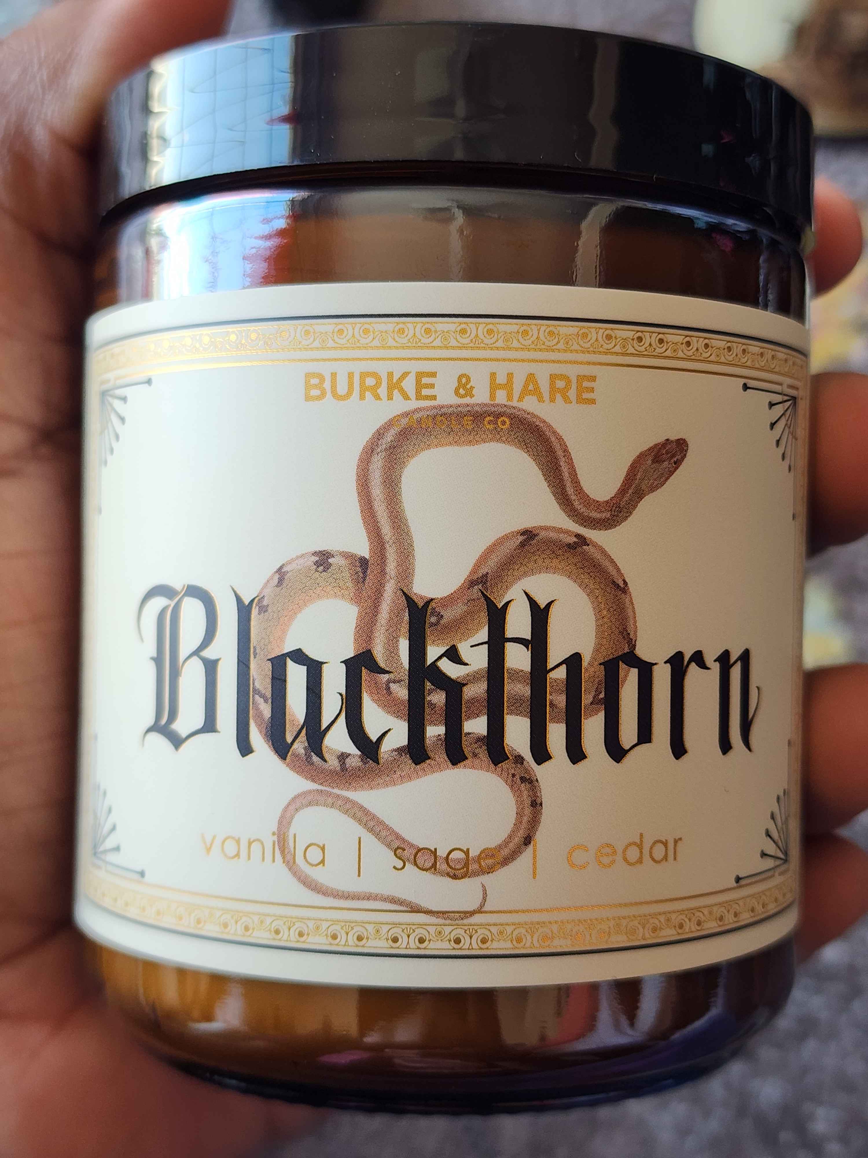 ID: an amber jar candle from Burke & Hare called Blackthorn, with notes of vanilla, sage, and cedar