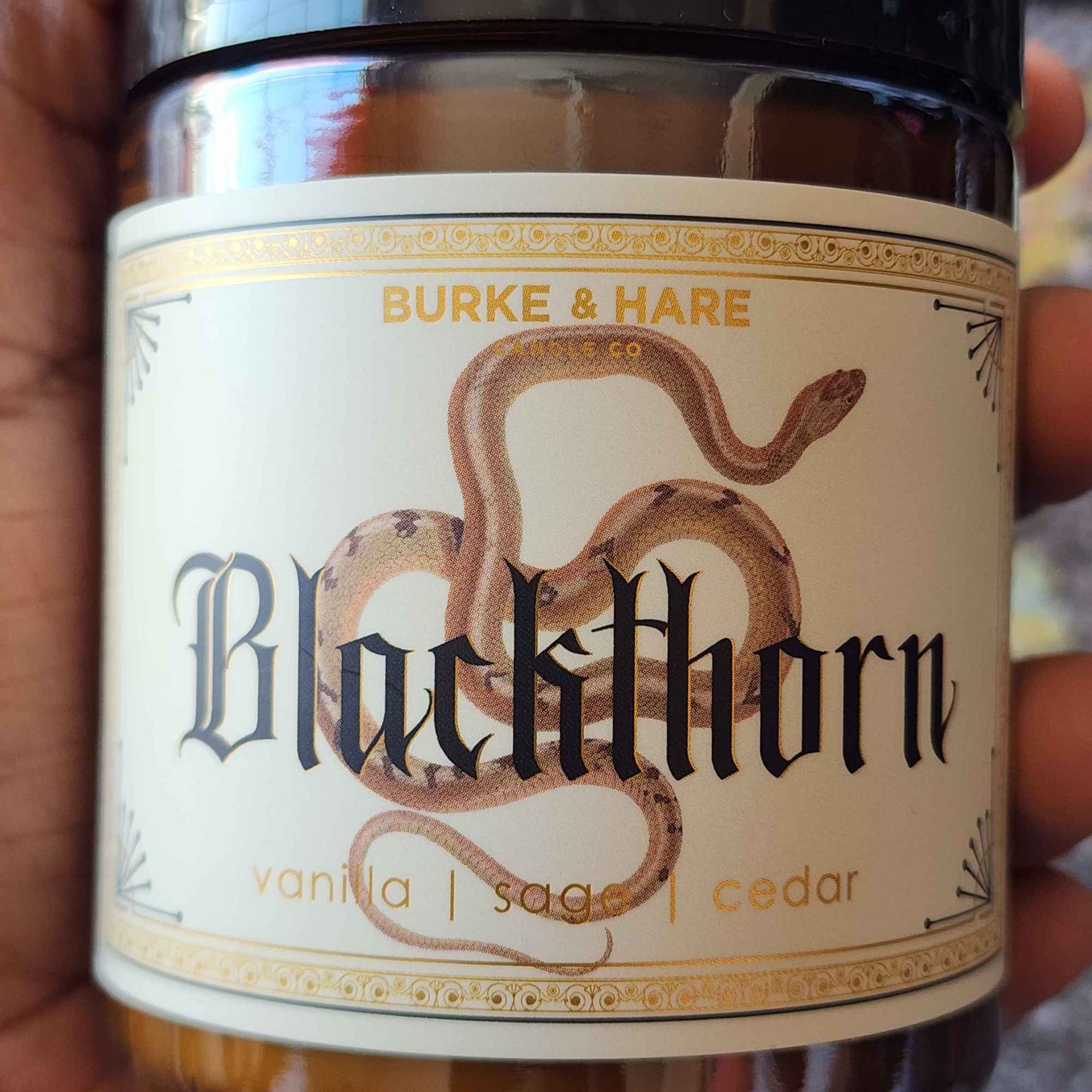 ID: an amber jar candle from Burke & Hare called Blackthorn, with notes of vanilla, sage, and cedar 