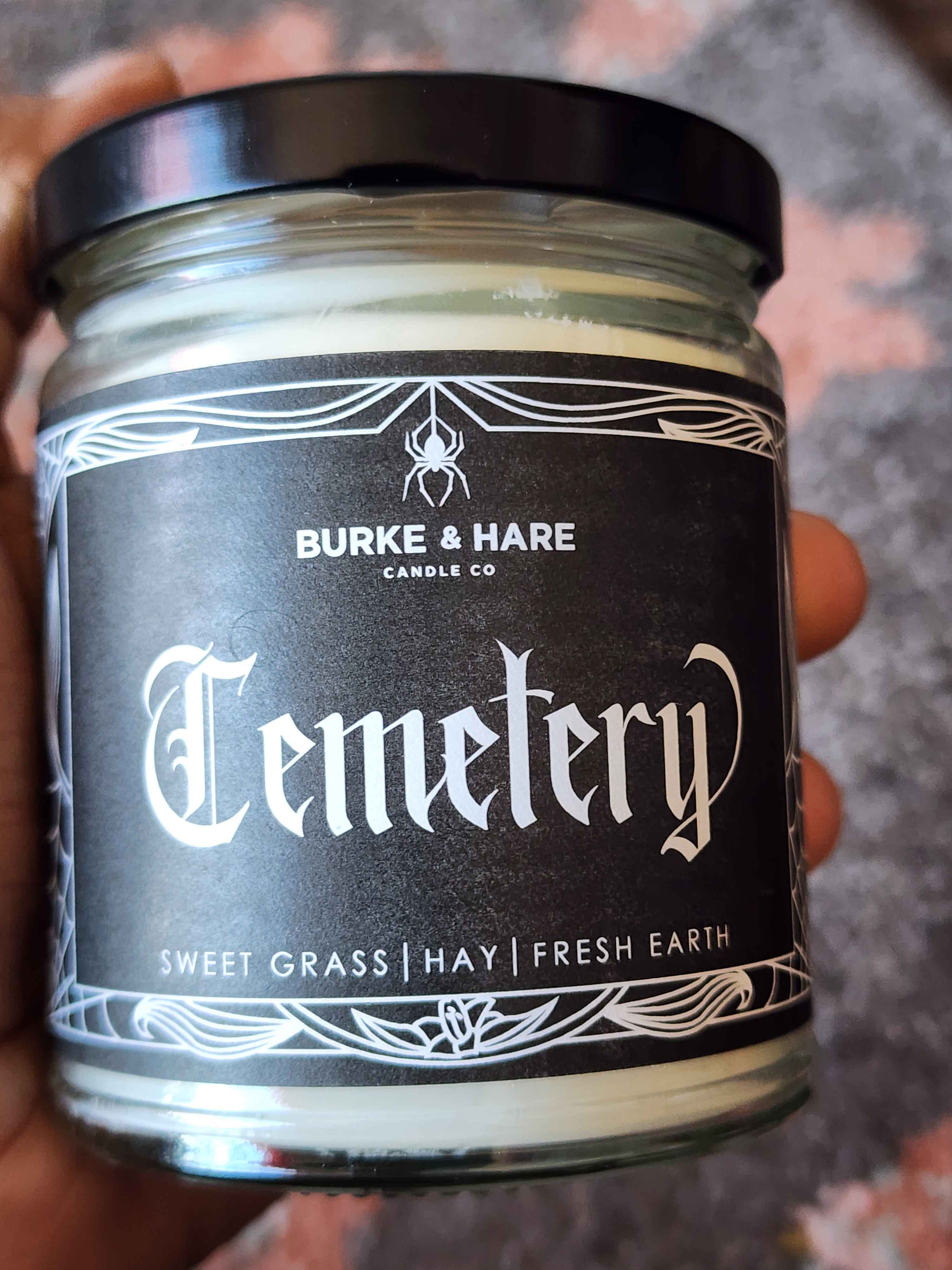 ID: a clear jar candle from Burke & Hare called cemetery, with notes of sweet grass, hay, and fresh earth.