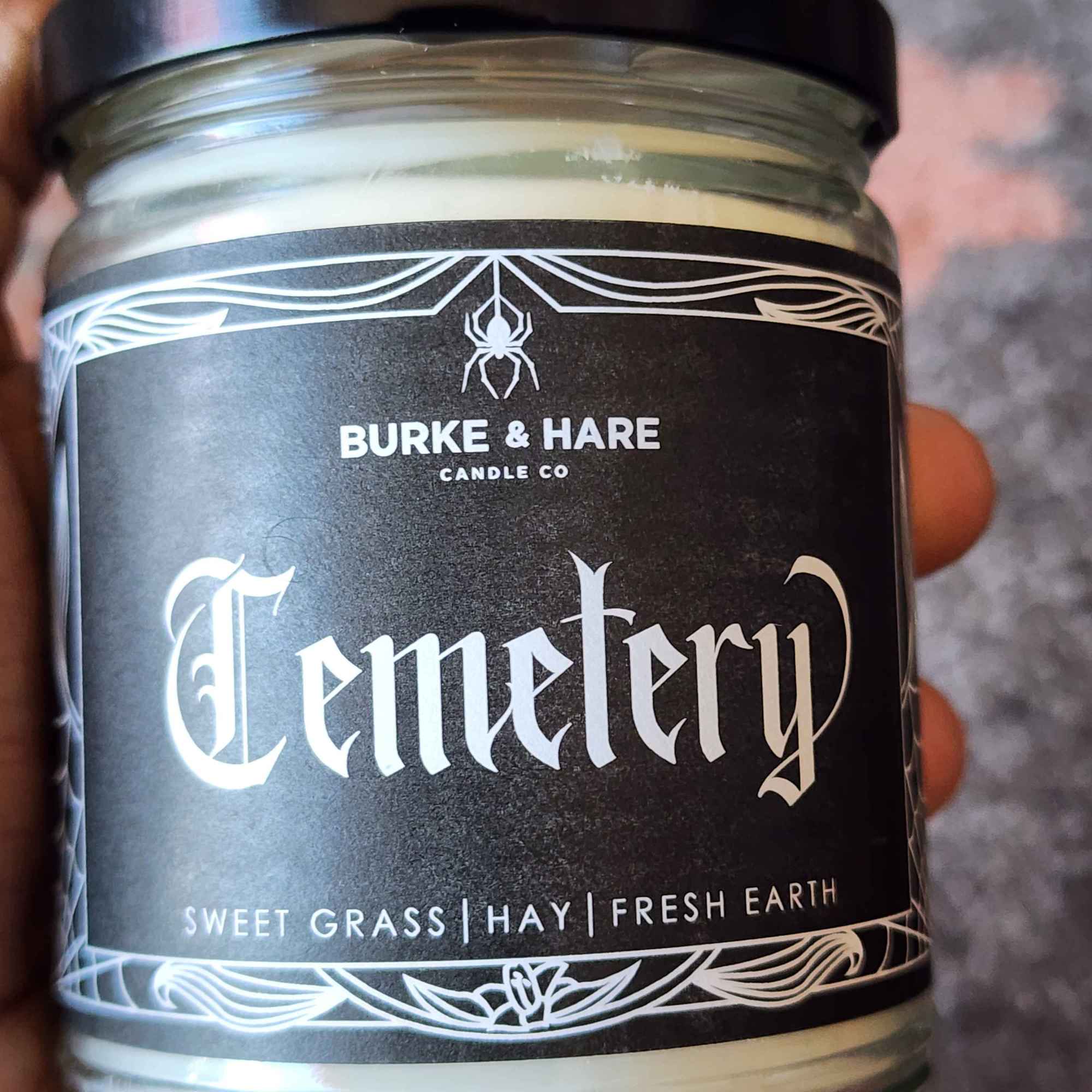 ID: a clear jar candle from Burke & Hare called cemetery, with notes of sweet grass, hay, and fresh earth. 