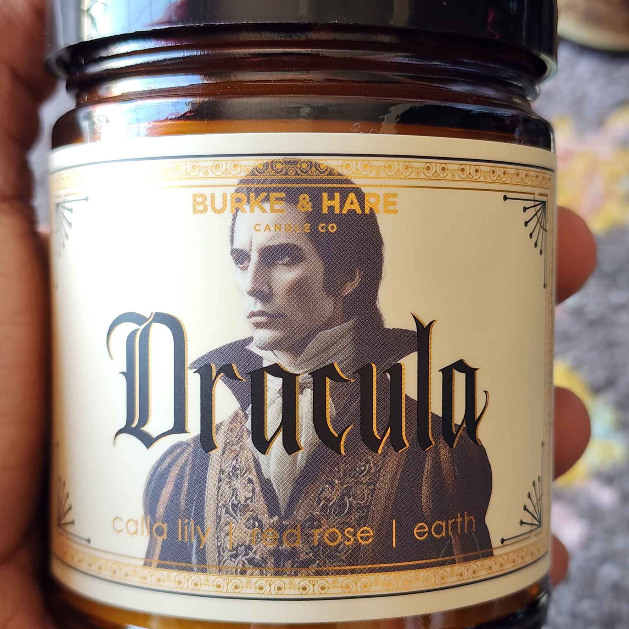 ID: an amber jar candle from Burke & Hare called Dracula, with notes of calla lily, red rose, and earth 