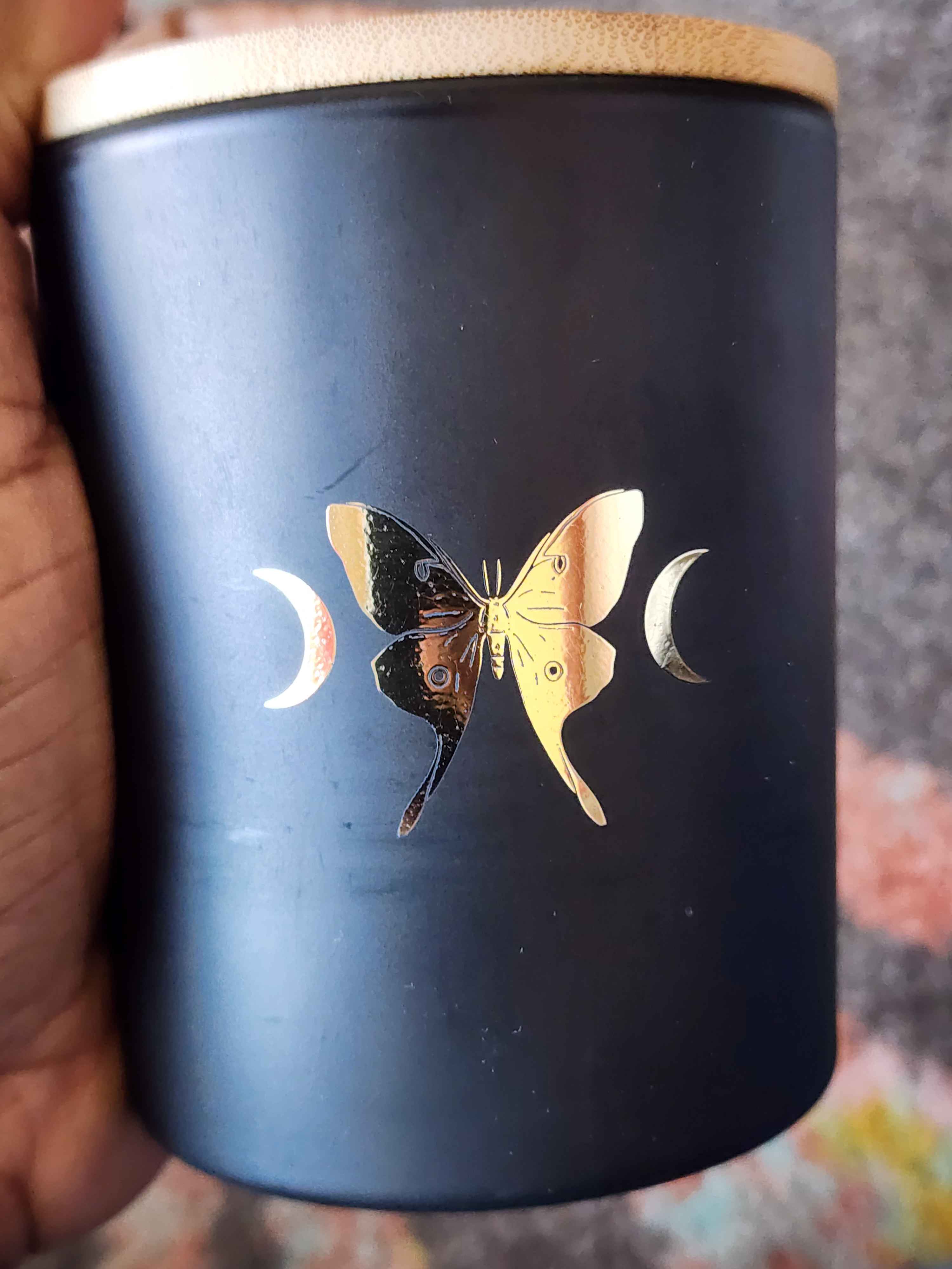 ID: a black jar candle from 13th Press called La Lune. a gold foil butterfly is on the jar, with crescent moons on either side