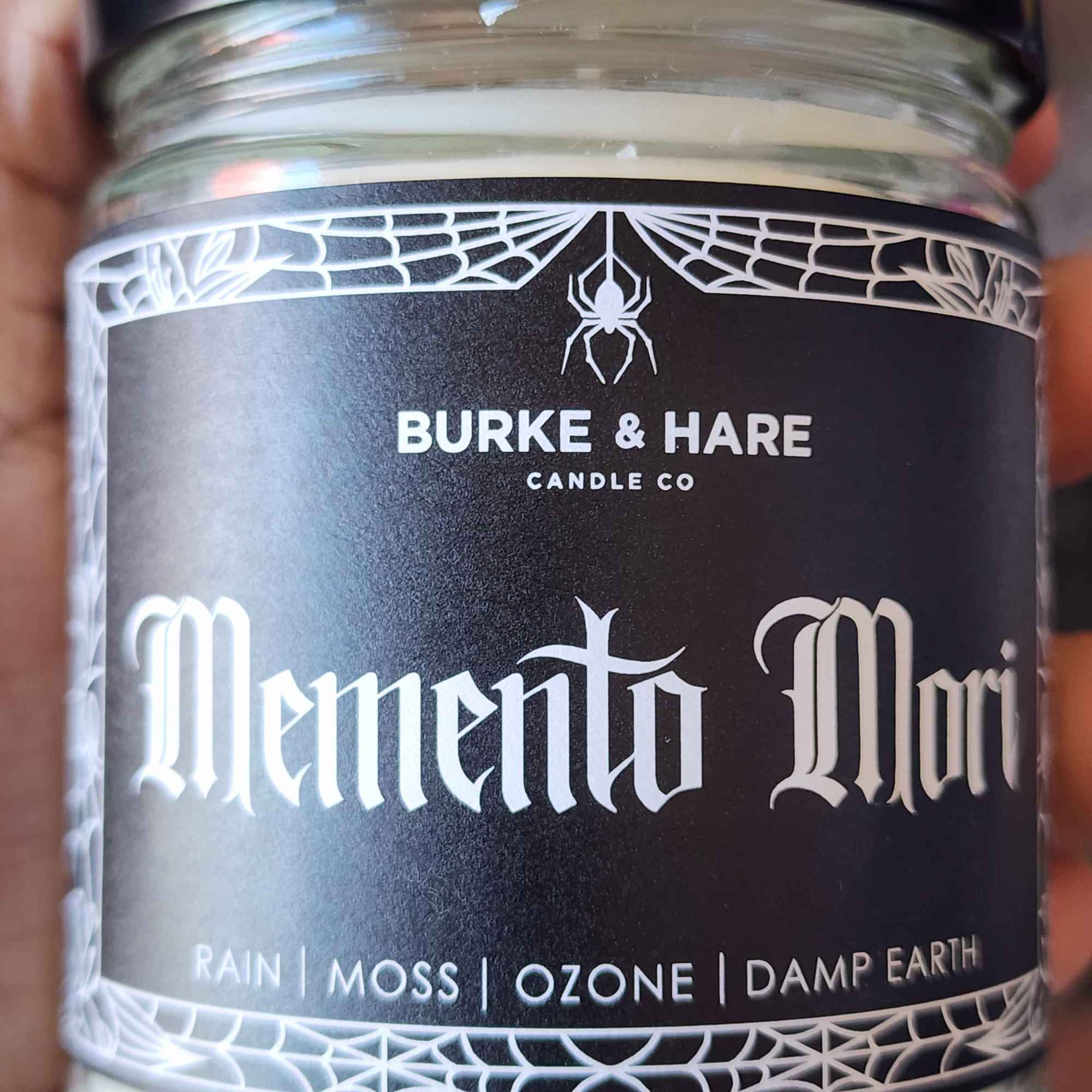ID: a clear jar candle from Burke & Hare called Memento Mori, with notes of rain, moss, ozone, and damp earth 