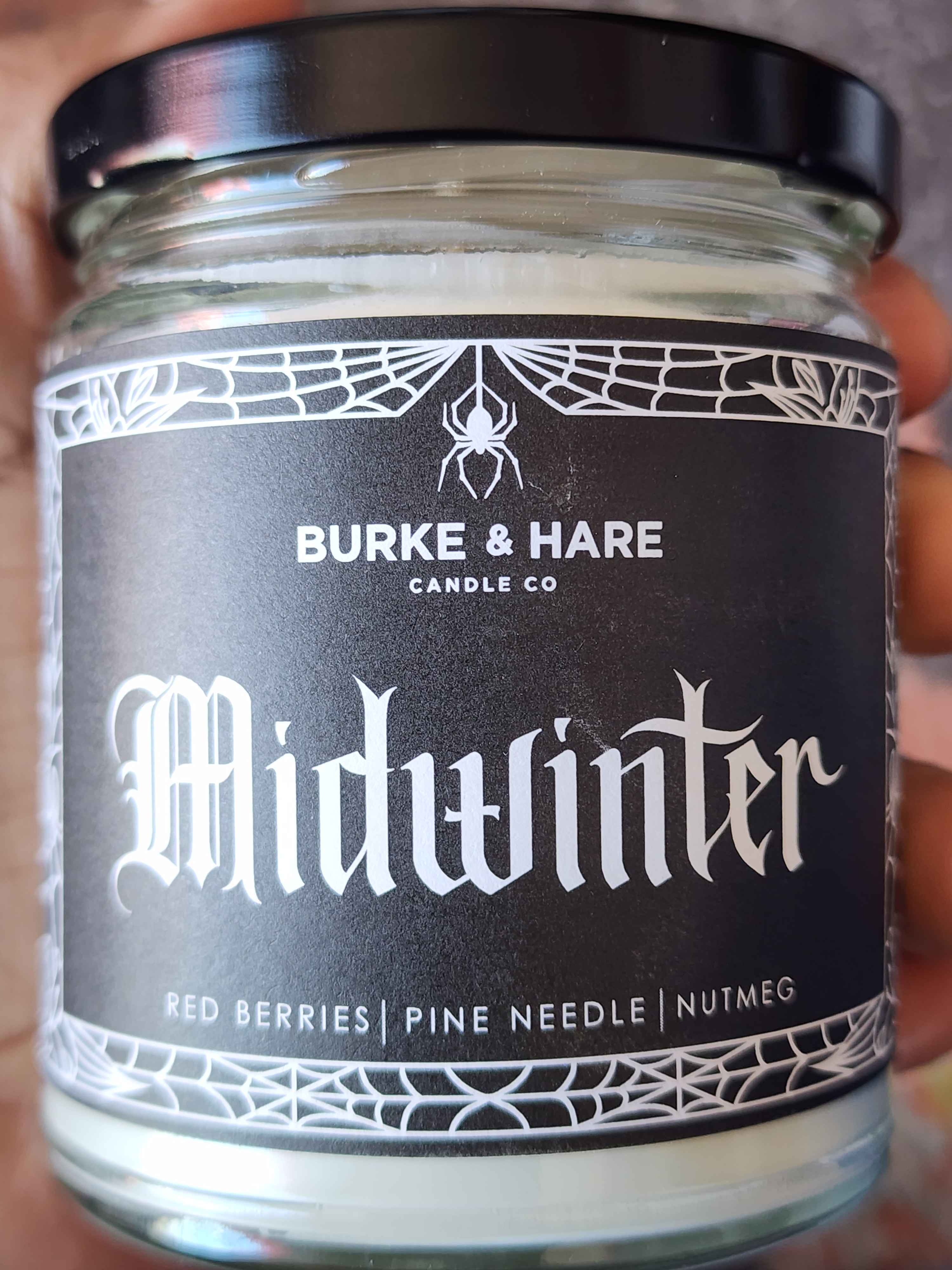 ID: a clear jar candle from Burke & Hare called Midwinter, with notes of red berries, pine needles, and nutmeg