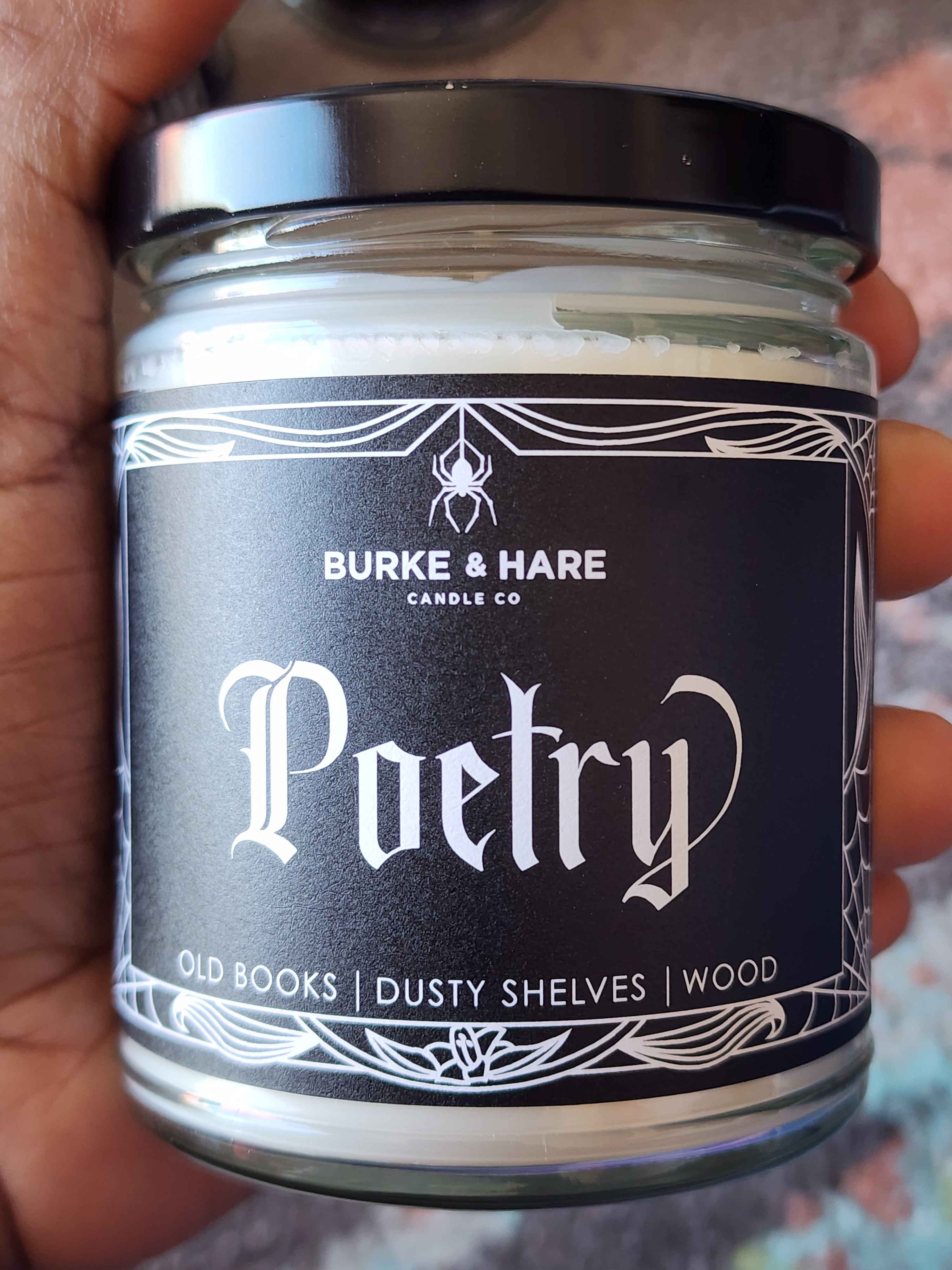 ID: a clear jar candle from Burke & Hare called Poetry, with notes of old books, dusty shelves, and wood