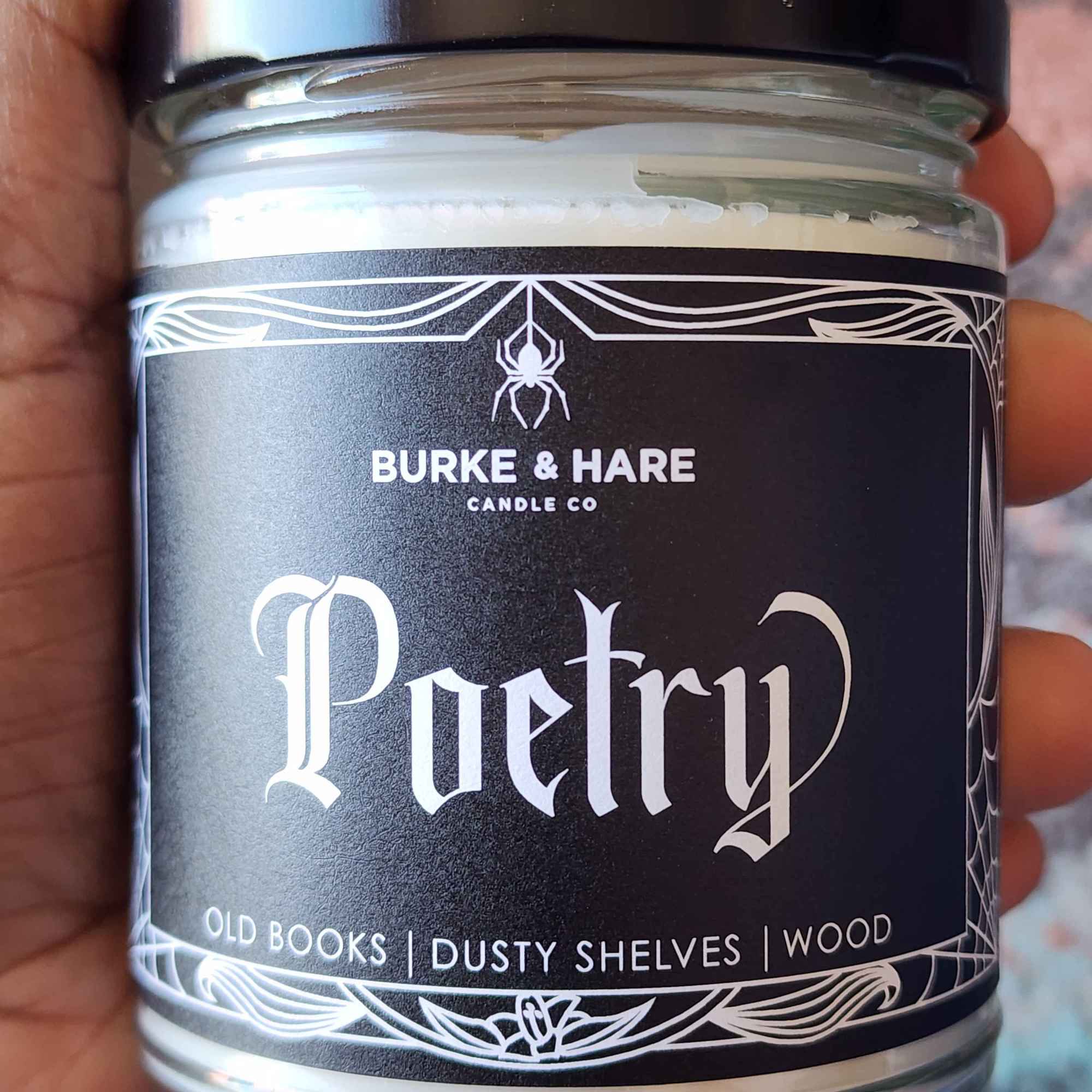 ID: a clear jar candle from Burke & Hare called Poetry, with notes of old books, dusty shelves, and wood