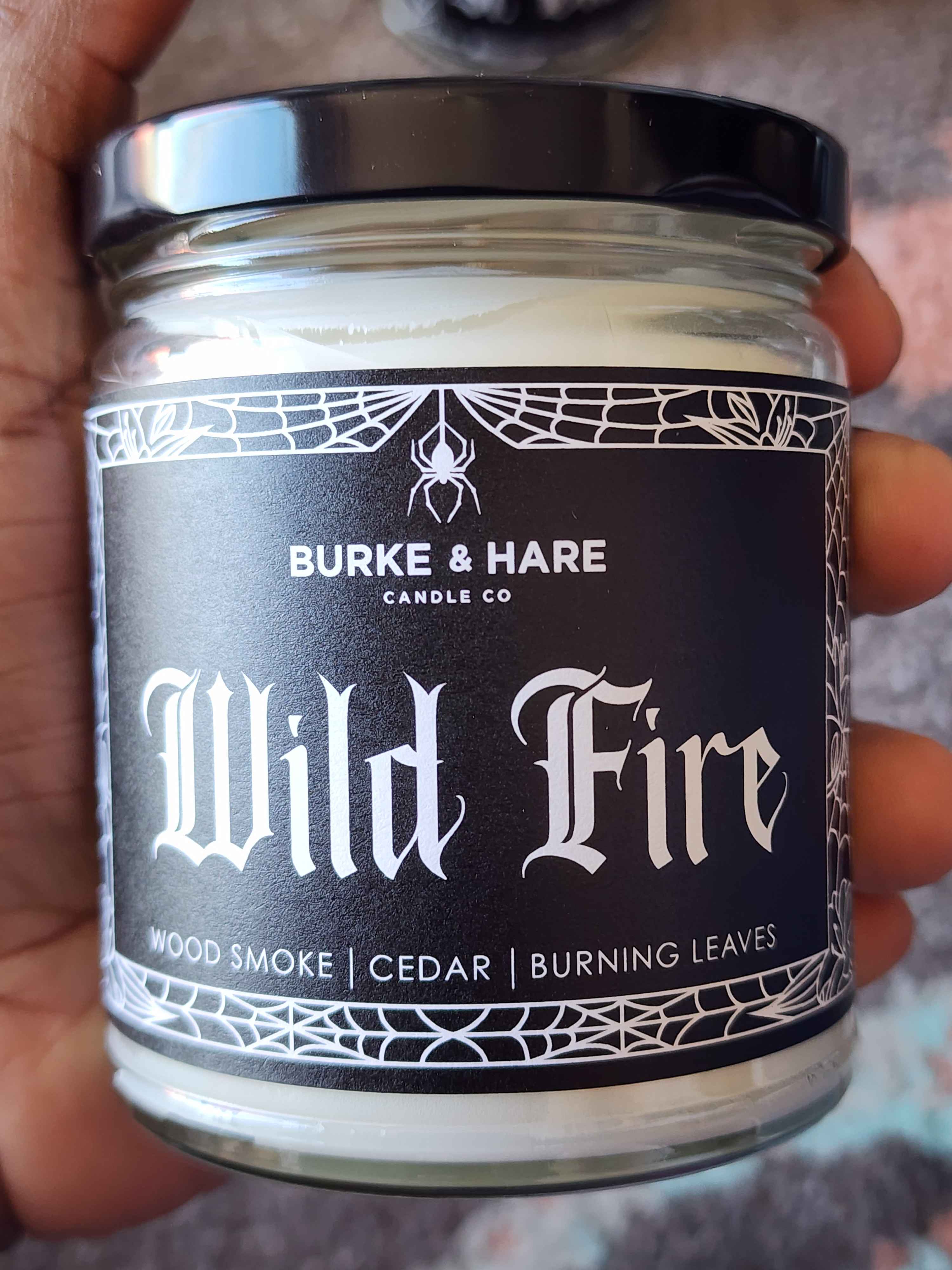 ID: a clear jar candle from Burke & Hare called Wild Fire with notes of woodsmoke, cedar, and burning leaves