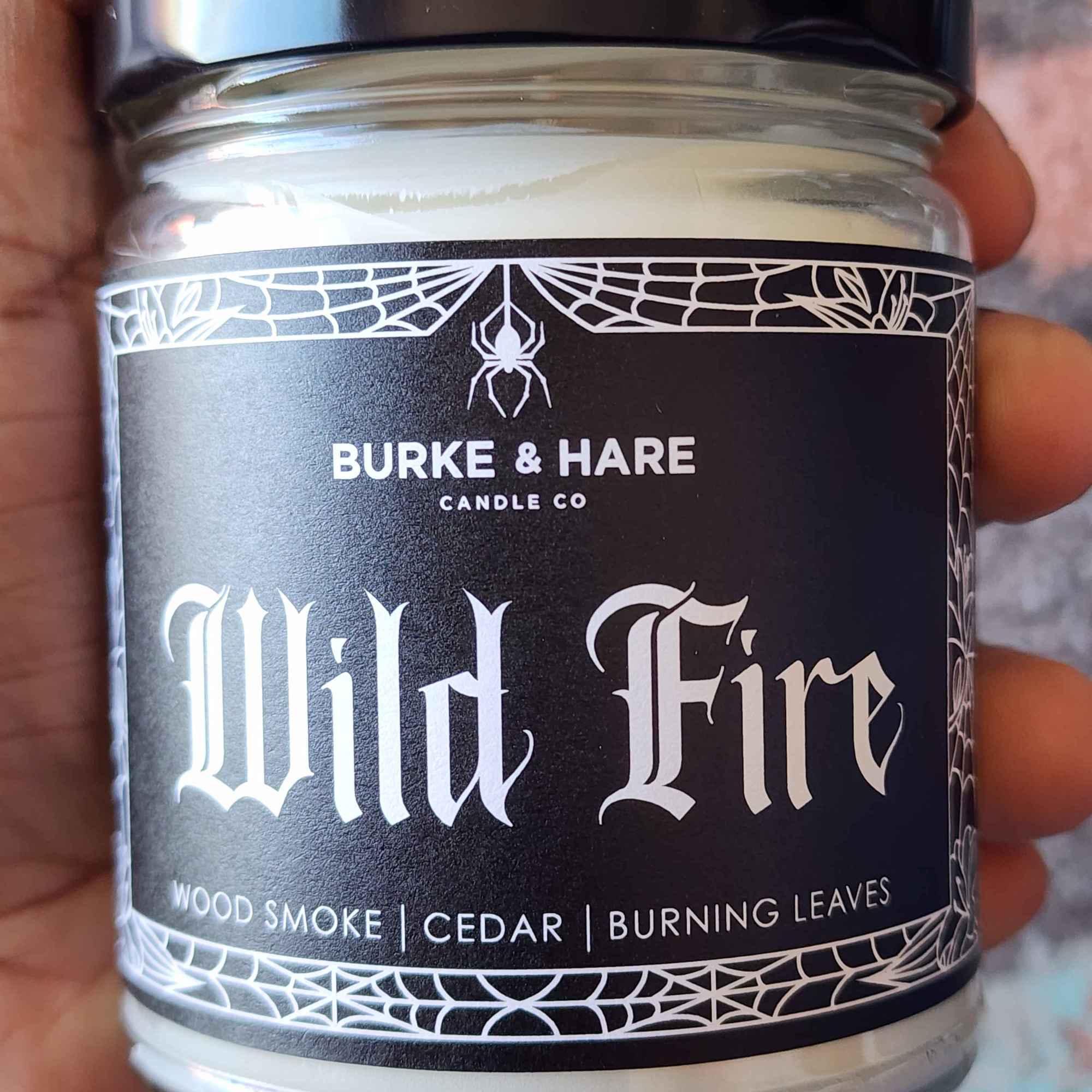 ID: a clear jar candle from Burke & Hare called Wild Fire with notes of woodsmoke, cedar, and burning leaves